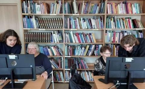 Du mokiniai bibliotekoje konsultuoja dvi pagyvenusias moteris
