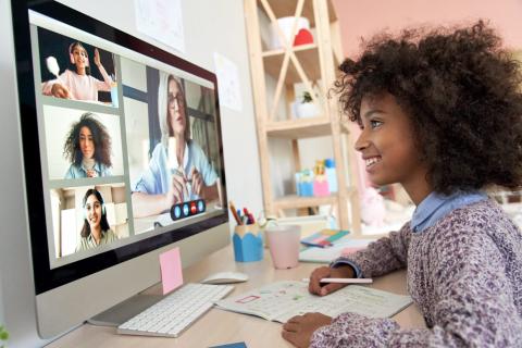 Mergaitė prie kompiuterio ekrano, kuriame matyti mokytoja ir internetinė klasė